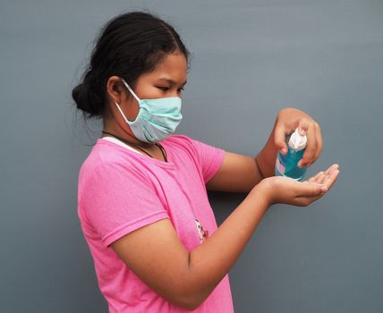 The girl is wearing a protective mask and pressing the alcohol gel to wash her hands.