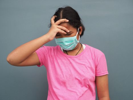 A girl wearing a protective mask With his hand on the temples Due to being sick.