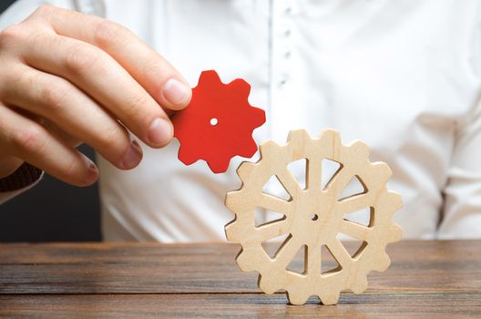 Businessman connects a small red gear to a large gear wheel. Symbolism of establishing business processes and communication. Increase efficiency and productivity. The best business formula for success