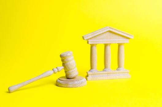 Wooden judge hammer and government building on a yellow background. Court. Concept of the state judicial system. Prohibitions and criminalization, repression, restriction of freedoms and rights