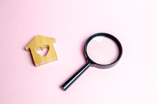 Wooden house with a heart and a magnifying glass. Search and purchase of affordable housing for young families and married couples. Mortgage. Rent a home for a romantic holiday on Valentine's Day.