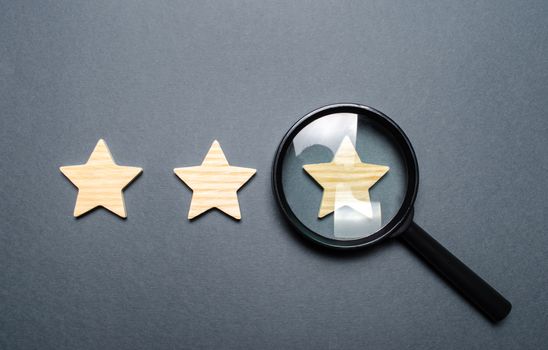 Three stars and a magnifying glass on a gray background. Authentication of the third star, rating fraud. Rating and status of the restaurant or hotel. Prestige.. High quality and reliability
