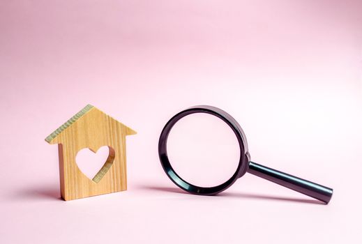 Wooden house with a heart and a magnifying glass. The concept of affordable housing for young families and married couples. Mortgage. Rent a home for a romantic holiday on Valentine's Day.