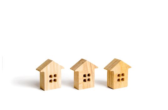 Three wooden figurines of houses on a white background. Minimalism and copy space. The concept of real estate, housing, buying or selling, renting. Settlement or community. Building construction.