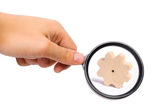 Magnifying glass is looking at the Wooden gear on a white background. Abstract background for presentations and banners. The concept of technology and industry, the think process. Part of a mechanism.