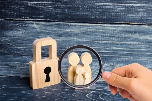 Magnifying glass is looking at the young family with children is standing near a wooden padlock. concept of a strong family, the continuation of the family. Loans for purchase of affordable housing