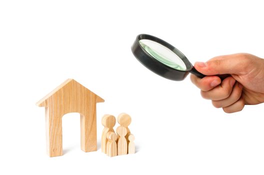 Magnifying glass is looking at the young family with children is standing near a wooden house. concept of a strong family, the continuation of the family. Loans for the purchase of affordable housing