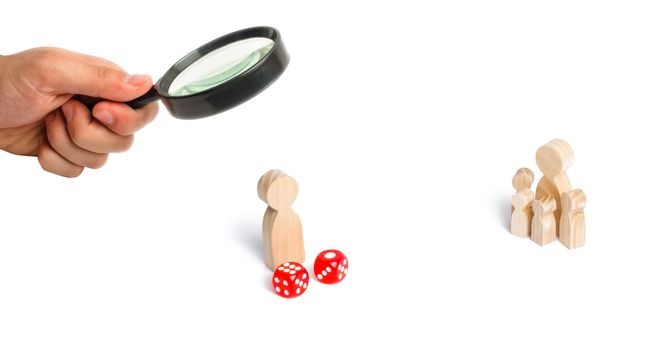 Magnifying glass is looking at the People are standing near dice. The concept of gambling, the dependence on gambling. Destruction of the family. RandomThe family stands near the dice cubes. .