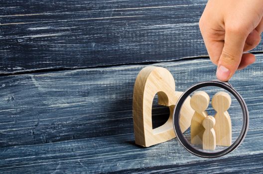 Magnifying glass is looking at the young family with a child is standing near a wooden heart. Love and loyalty, a strong young family. Family relationships. Civil marriage. Love, affection, sympathy