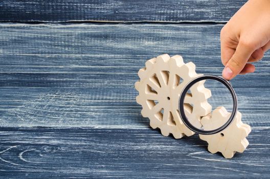 Magnifying glass is looking at the Gears of wood stand on a dark wooden background. Concept of technology and industry, engineering. Mechanical parts. Innovations and new technologies in the industry.