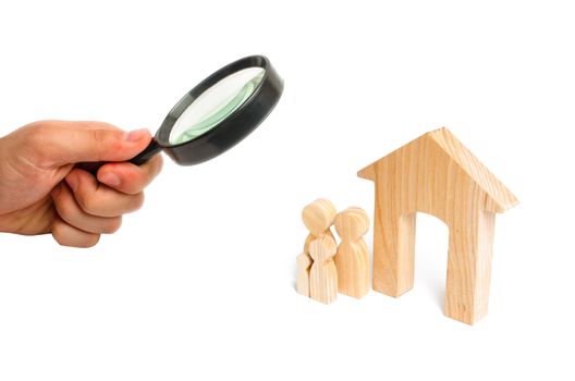 Magnifying glass is looking at the young family with children is standing near a wooden house. A new house for the family. The concept of a strong family, the continuation of the family.