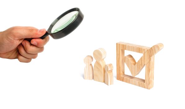 Magnifying glass is looking at the Three wooden human figures stand together next to a tick in the box. Volunteers, parties, candidates. Human rights. The concept of elections and social technologies.
