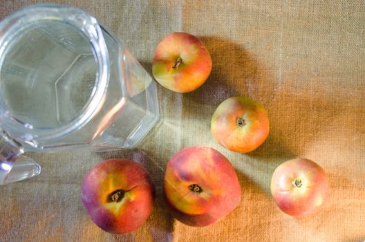 apples, peaches and a jug of water on a rough cloth background