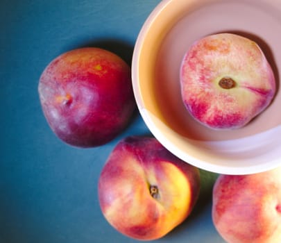 summer round peaches on a blue sea background and flattened fig peach in a round bowl, top view