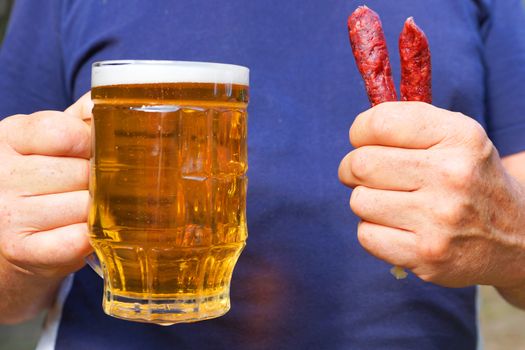 a mug with beer and sausages in the hands of a man close up