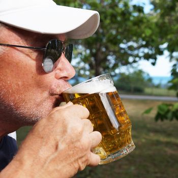 man drinks beer from a large glass mug in nature, close-up
