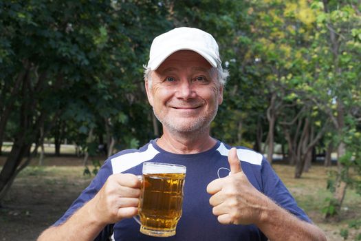 a laughing man holds a mug of beer in one hand, with the other hand shows that everything is fine in the park