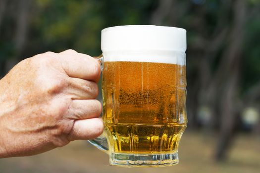 glass mug with beer and foam in a man's hand on the background of nature close up