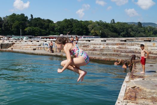 Varna, Bulgaria - July, 19, 2020: girl jumping into the sea from the pier.