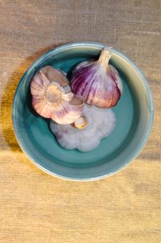 heads of garlic in an azure bowl, top view on a background of rough fabric with lights and shadows