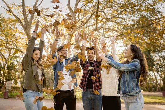 Group of friends in the park having fun throwing leaves in the air