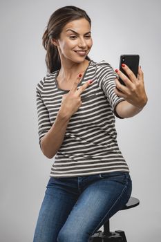 Beautiful happy young woman sitting on a bench and makign a selfie