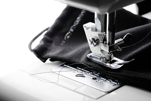 An all black face covering is stitched in a sewing machine. Blank white copy space to the left hand side. Contrasty image.