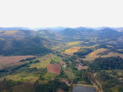 Aerial View of green scenic forest and land in the mountain in tropical country. Aerial view of forest to make with farm field and villa. Green area in the forest with lake