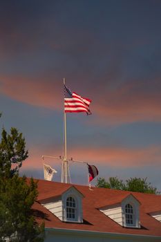 The American flag flying against a clear blue sky over a red roof with dormers