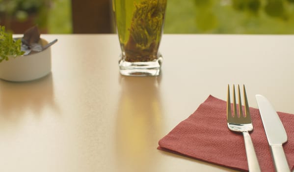 Close up table set for breakfast. Fork and knife on a napkin, a bottle of olive oil and herbs in a bowl