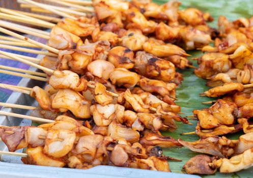 Squid skewers waiting to be grilled in charcoal grill. Thai delicious street food in local market.