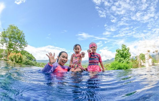 Asian sibling sisters playing in swimming pool with family in a hot summer day. Family lifestyle in vacation.