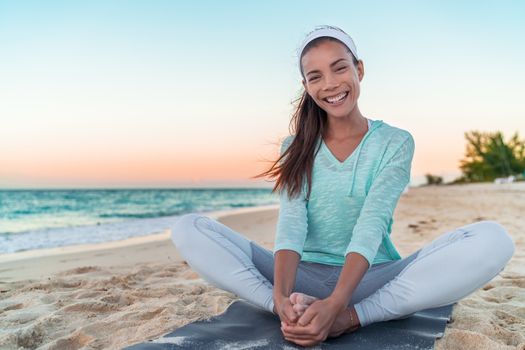 Happy healthy lifestyle yoga girl stretching legs exercise on morning fitness training. Asian woman smiling on beach.