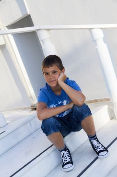 the teenager sitting on the steps with his head on his palm and smiles