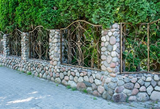 beautiful patterned wrought iron fence with stone pillars on sunny summer day