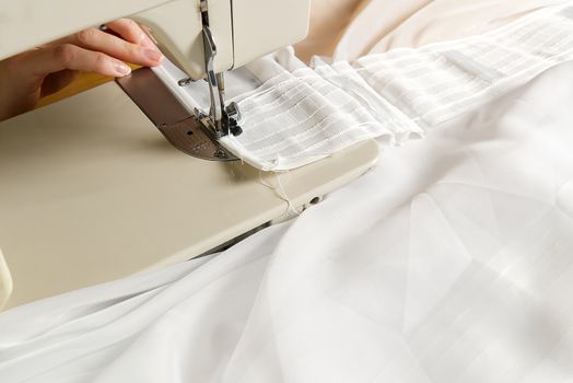 A woman works on a sewing machine. seamstress sews white curtains, close up view