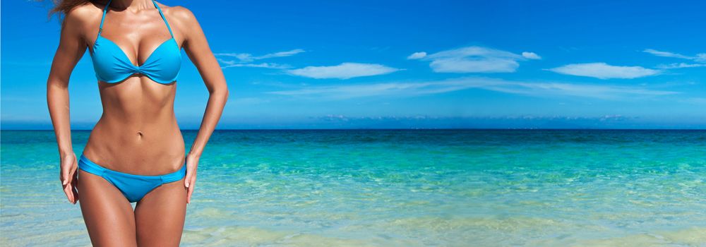 Woman with perfect body in blue bikini over tropical sea background