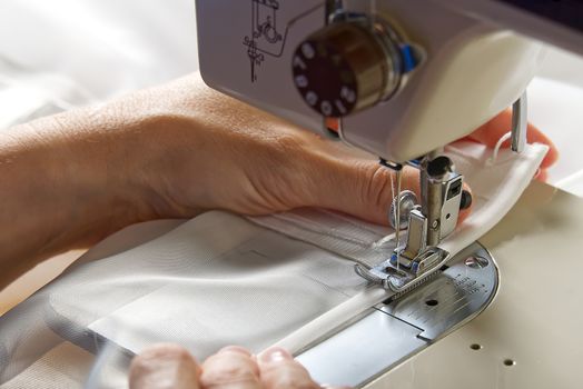 A woman works on a sewing machine. seamstress sews white curtains, close up view