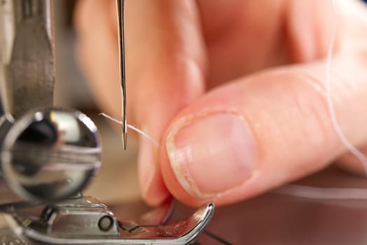 woman threading a needle on a sewing machine. close up, selective focus