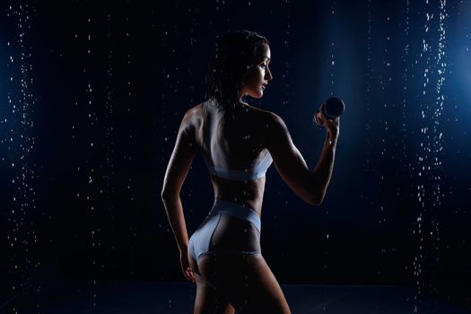 athletic woman pumping up muscles with dumbbells Beautiful athletic caucasian woman lifts dumbbells in aquastudia against a background of splashing water. Freshness sport motivation