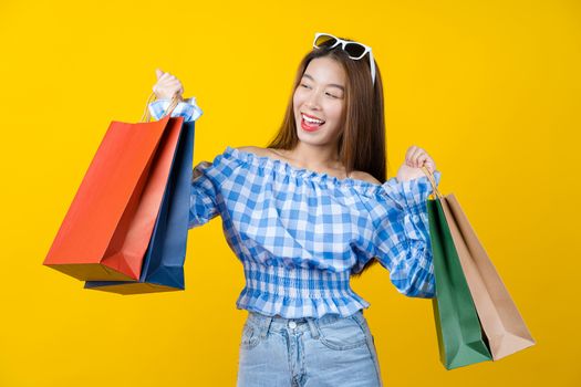 Attractive Asian smiling young woman Carrying shopping coloful bag on aisolated yellow color background, copy space and studio, black friday season sale concept.