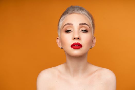 Close up fashion portrait woman with short hair red lips and naked shoulders on the colored orange background.