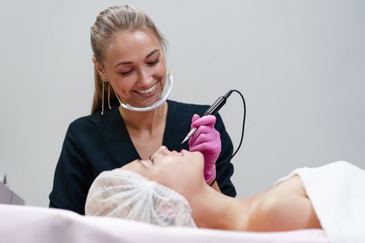 Cosmetology cabinet client lies on couch. Beautician applies permanent ink on lips. Procedure of permanent lip makeup. Free space. Beauty industry