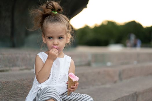 Little caucasian girl 3 years old eats ice cream closeup portrait. Summertime. Childhood Child with frozen dessert in hand walking outdoor. Close up portrait european girl witn ice-cream.