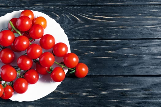 Cherry tomatoes in the white plate on the dark wooden table. Juicy ripe vegetables on a black background. Healthy eating. vegetarian food