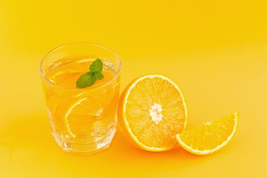 Detox Water with orange in a glass on an orange background.