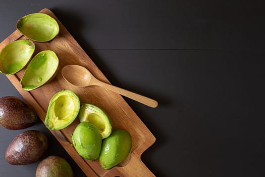 Fresh organic avocado sliced in half on black wooden table.