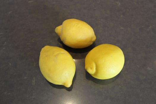 Three whole yellow lemons on a gray stone surface