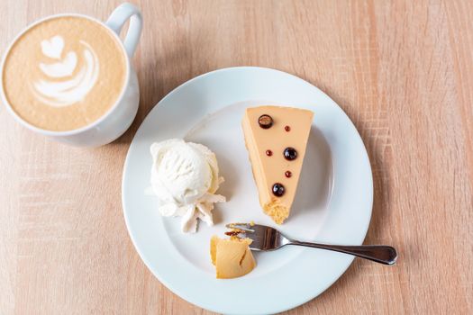 A piece of caramel cheesecake served with ice cream and a cup of cafe latte, flat lay