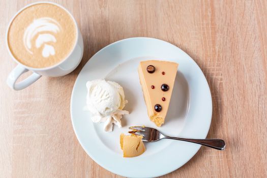 A piece of caramel cheesecake served with ice cream and a cup of cafe latte, flat lay